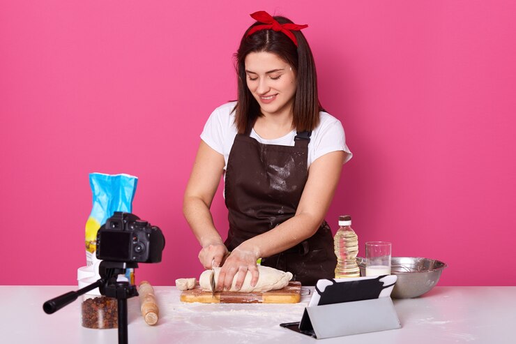 Foto gratuito mujer cocinando en la cocina, cortando un pastel crudo con un cuchillo, obteniendo placer durante el proceso, teniendo un tazón, aceite, tabla