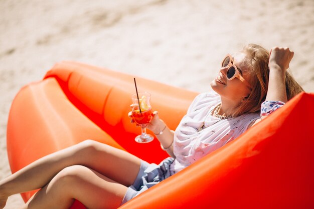 Mujer con coctail tumbado en un colchón de la piscina en la playa