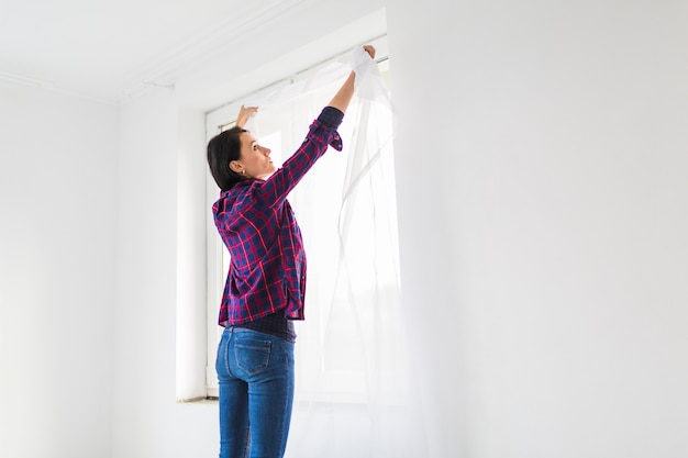 Mujer colgando cortinas en la ventana