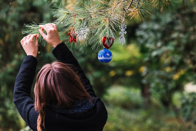 Mujer colgando juguetes de Navidad en ramita en bosque