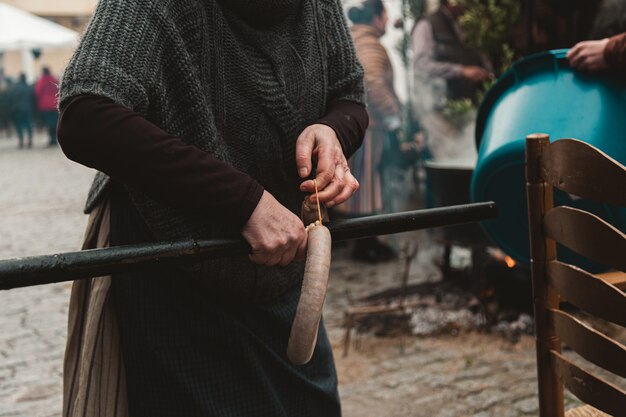 Mujer colgando kielbasa de un tubo rodeado de gente