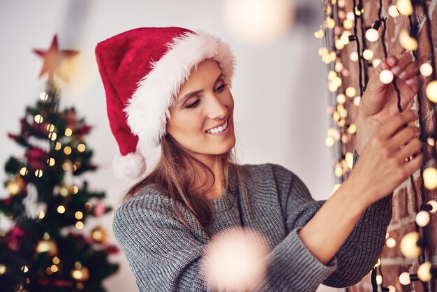 Mujer colgando luces de Navidad en casa