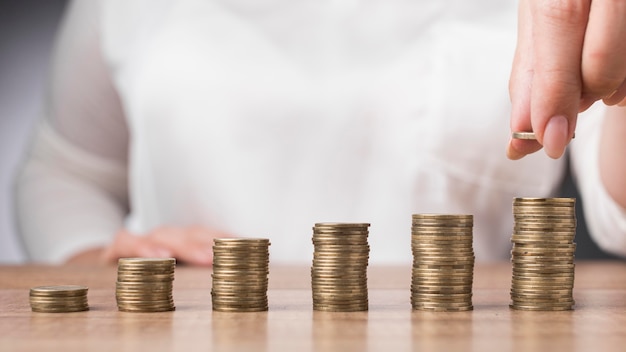 Mujer colocando una moneda sobre un montón de monedas