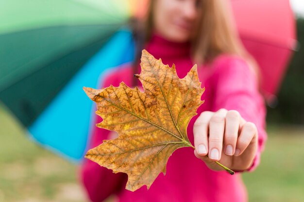 Mujer con coloridos paraguas sosteniendo una hoja de otoño