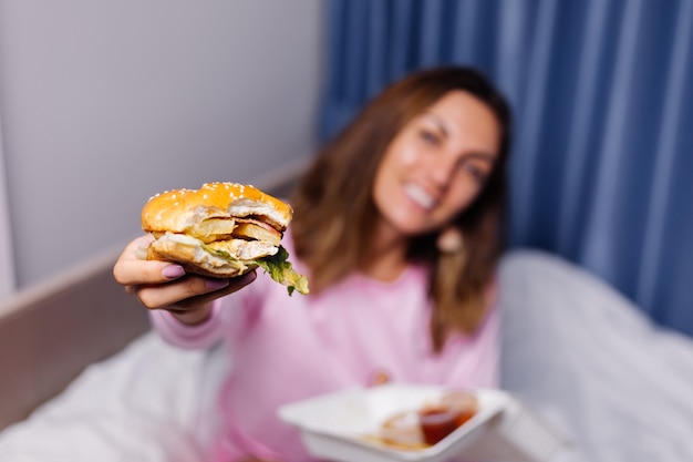 Mujer come hamburguesa en casa