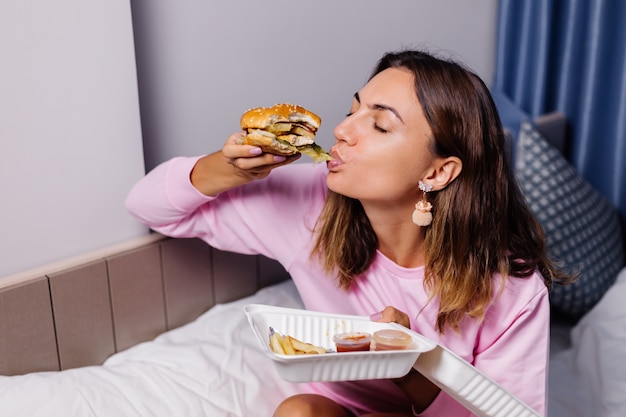 Mujer come hamburguesa en casa