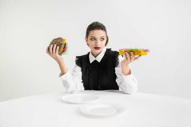 Mujer come hamburguesa y hot-dog de plástico, concepto ecológico.