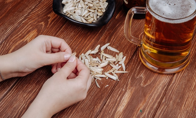 Una mujer come semillas de girasol aperitivo salado con una jarra de cerveza en vista lateral de madera rústica