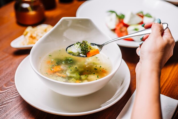 Mujer come sopa de vegetales con brócoli, zanahoria, apio y papa