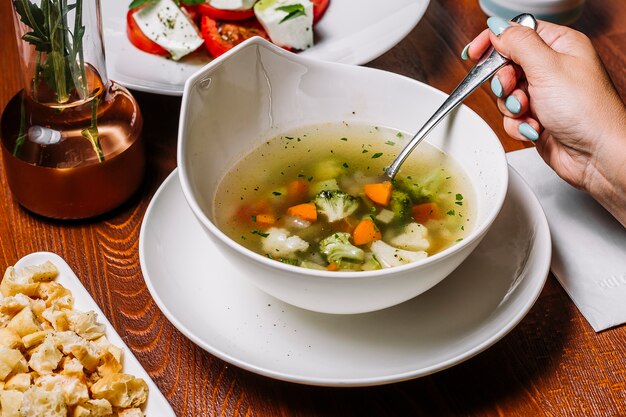 Mujer come sopa de verduras con brócoli, guisantes, zanahoria, apio y papa