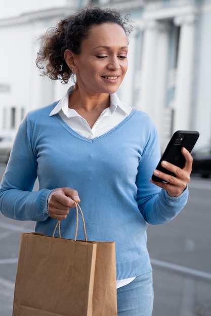 Mujer con comida para llevar en bolsas de papel con smartphone en la calle