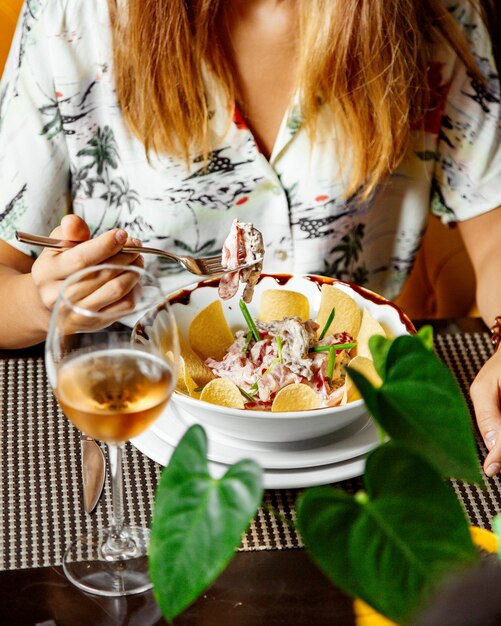 Mujer comiendo ensalada de carne con rodajas de tomate juliana servido con patatas fritas