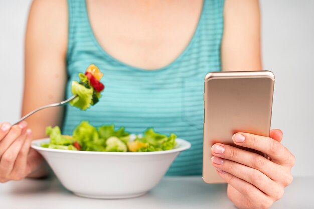 Mujer comiendo una ensalada y mirando el teléfono