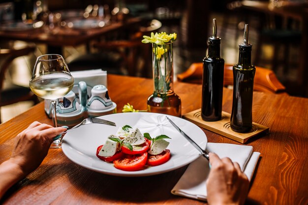 Mujer comiendo ensalada de tomate con mozzarella y menta servida con vino blanco