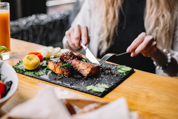Una mujer comiendo filete de pescado al horno con hierbas y verduras en la mesa