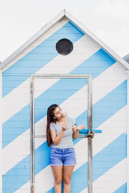 Foto gratuita mujer comiendo helado enfrente de casa de madera en la playa