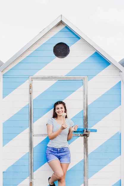 Mujer comiendo helado enfrente de casa de madera en la playa