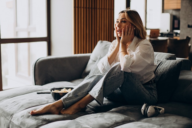 Mujer comiendo palomitas de maíz en casa en el sofá y viendo la película