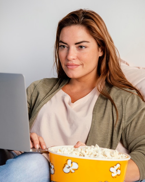 Foto gratuita mujer comiendo palomitas de maíz mientras ve la película en la computadora portátil