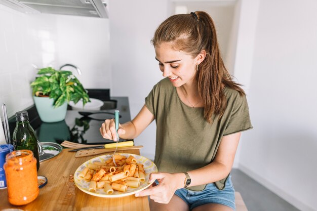 Mujer comiendo pasta con tenedor en la cocina