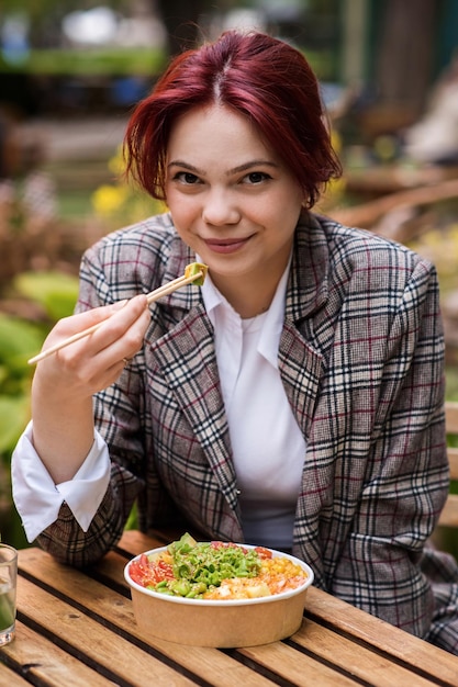 Una mujer comiendo un poke en un parque