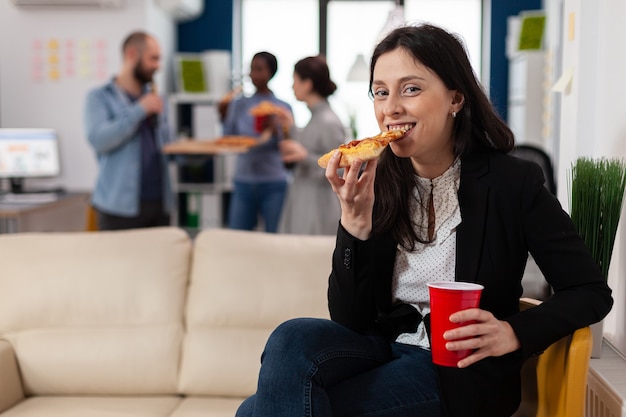 Mujer comiendo una rebanada de pizza en la fiesta después del trabajo con amigos