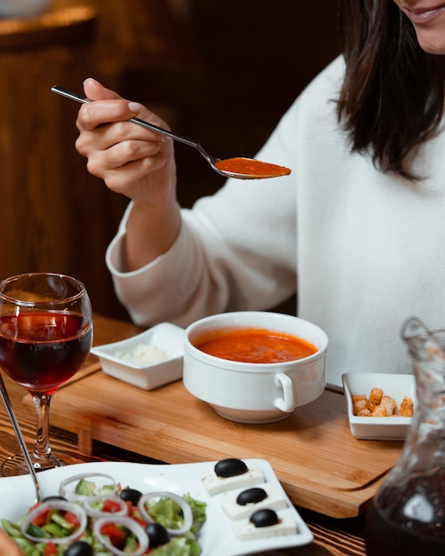 mujer comiendo sopa de tomate con relleno de pan, una copa de vino