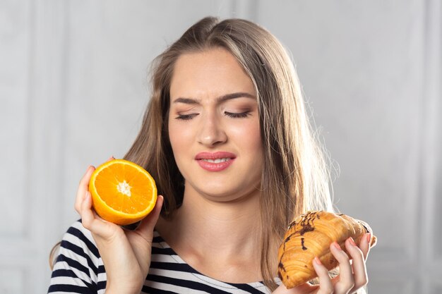 Mujer comparando torta malsana y fruta naranja