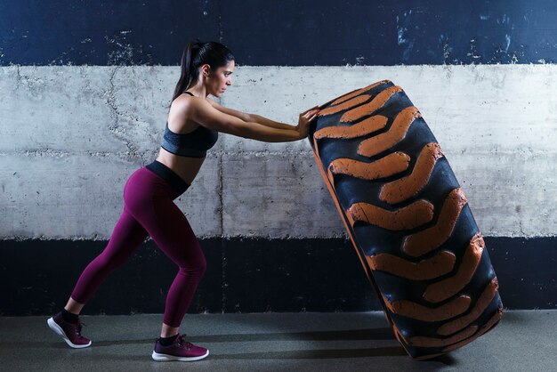 Mujer de complexión muscular que se resuelve en el gimnasio volteando el neumático del camión