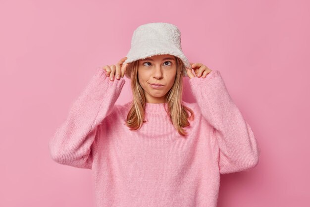 Mujer compra un nuevo sombrero de piel blanca se viste para caminar al aire libre viste un jersey de gran tamaño cálido posa en rosa