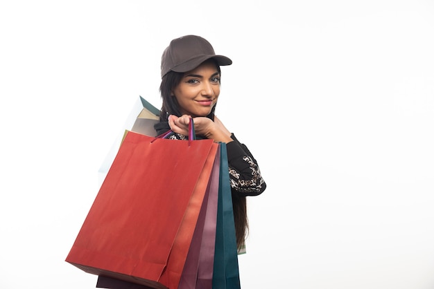 Mujer de compras con gorra mostrando bolsa de compras en la pared blanca