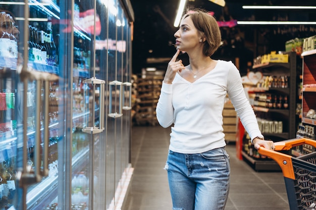 Mujer de compras en la tienda de comestibles, junto al refrigerador