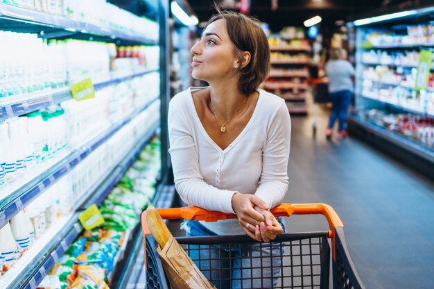 Mujer de compras en la tienda de comestibles, junto al refrigerador