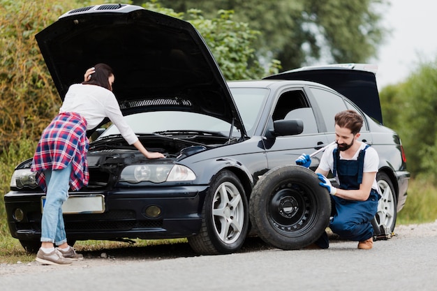 Foto gratuita mujer comprobando motor y hombre cambiando neumáticos