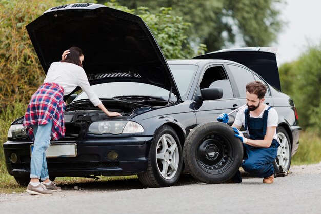Mujer comprobando motor y hombre cambiando neumáticos