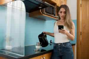 Foto gratuita mujer comprobando su teléfono mientras pone café en una taza