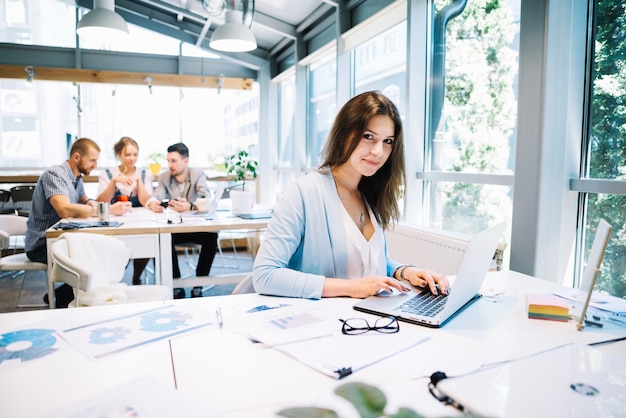 Mujer en la computadora portátil que mira la cámara