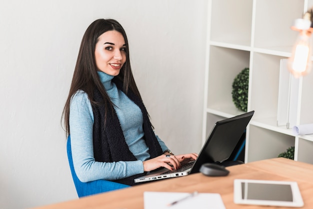 Mujer con la computadora portátil que mira la cámara