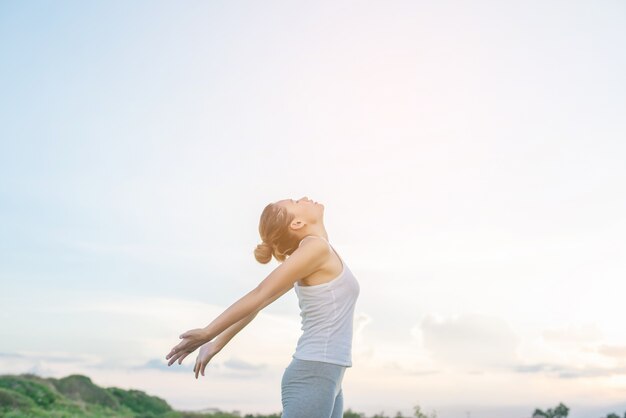 Mujer concentrada estirando sus brazos con el cielo de fondo