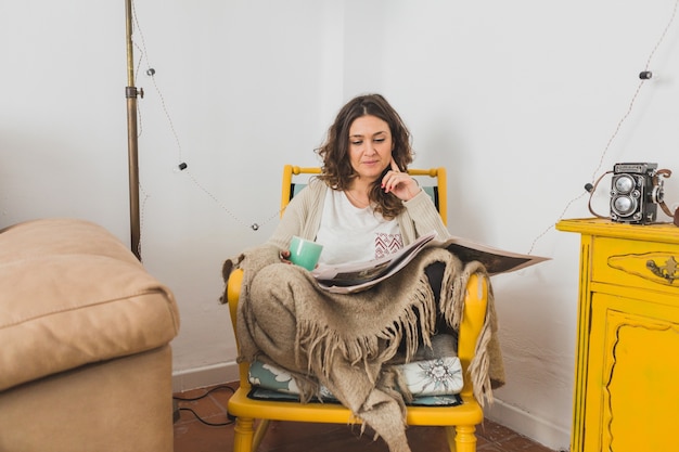 Mujer concentrada leyendo el periódico sentada en una silla