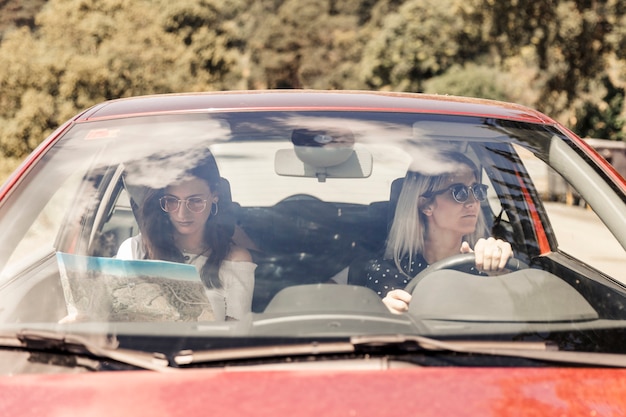 Mujer conduciendo el coche con su amiga mirando el mapa