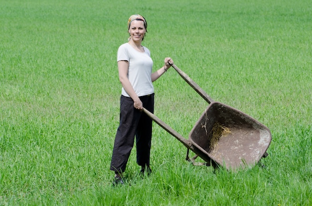 Mujer confiada que trabaja con una carretilla de mano en una granja
