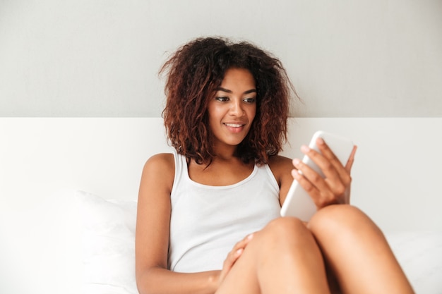 Mujer confiada sonriente que charla en smartphone en casa