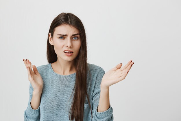 Mujer confundida y perpleja levanta las manos consternada