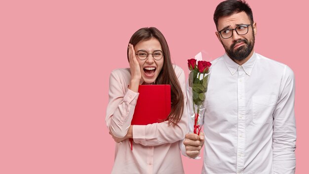 La mujer contenta y llena de alegría tiene la primera cita, expresa emociones positivas, un tipo incómodo se encuentra cerca con un ramo de rosas