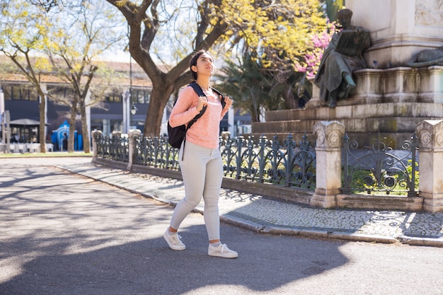 Mujer contenta con mochila y caminando por la ciudad