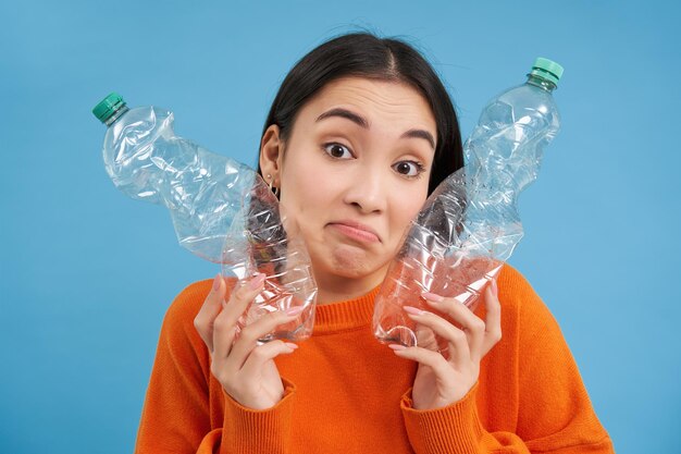 Una mujer coreana pensativa muestra dos botellas de plástico que parece un concepto despistado y desconcertado de reciclar un