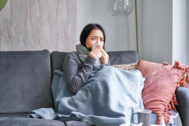 La mujer coreana se siente mal estornudando y tosiendo resfriada quedándose en casa con fiebre y tempera