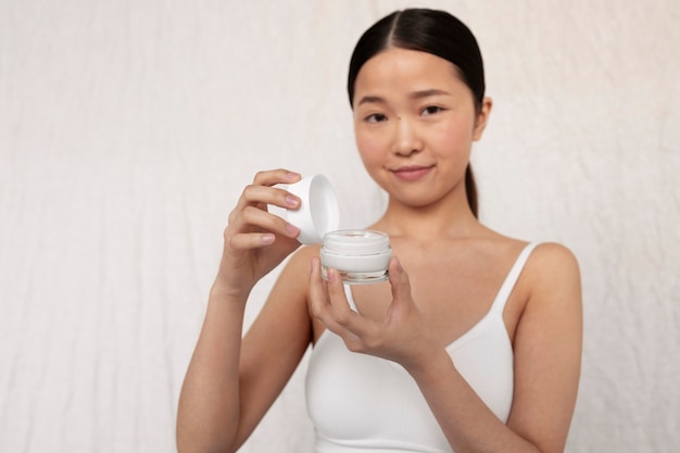 Mujer coreana de tiro medio posando con crema para la cara