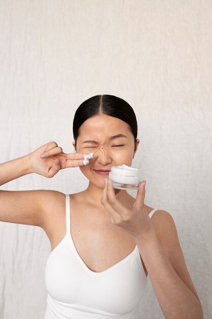 Mujer coreana de tiro medio posando con crema para la cara